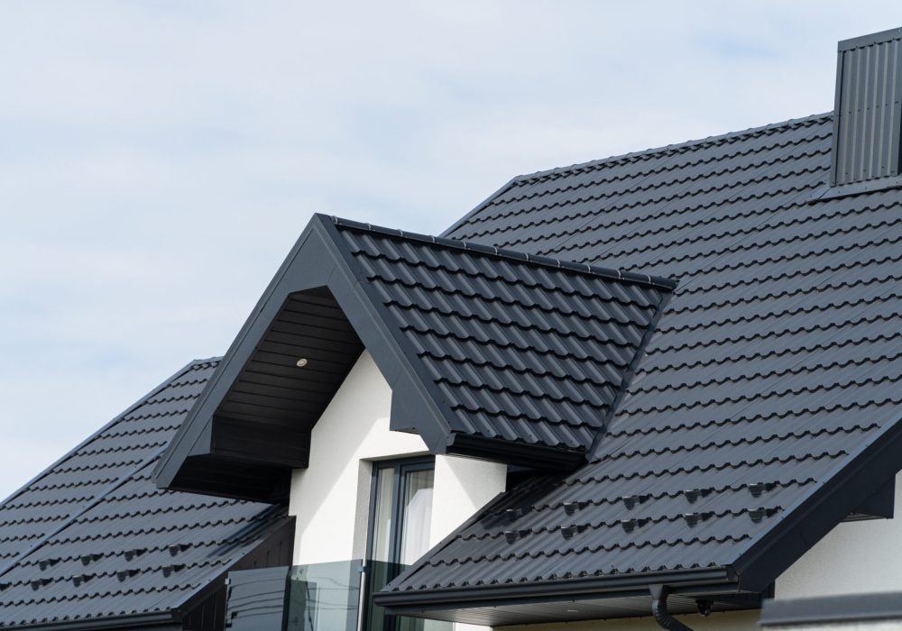 A beautiful modern house is covered with black metal tiles. Roofing of metal profile wavy shape.